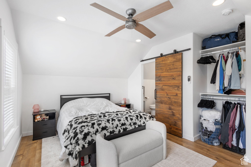 Bedroom featuring a barn door, recessed lighting, lofted ceiling, wood finished floors, and multiple windows