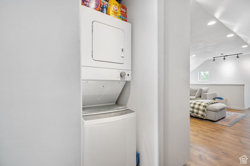 Laundry room with baseboards, recessed lighting, wood finished floors, stacked washer and clothes dryer, and laundry area