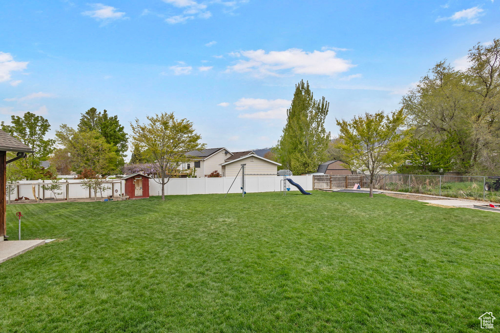 View of yard with a storage unit, an outbuilding, a fenced backyard, and a playground