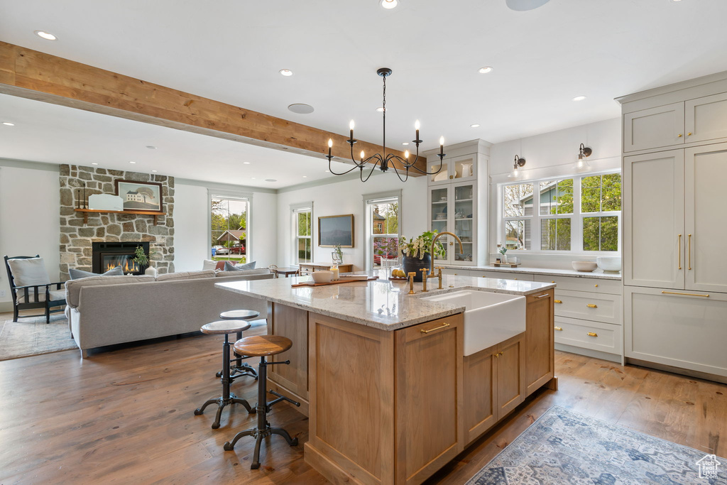 Kitchen featuring recessed lighting, wood finished floors, a sink, light stone countertops, and a kitchen island with sink