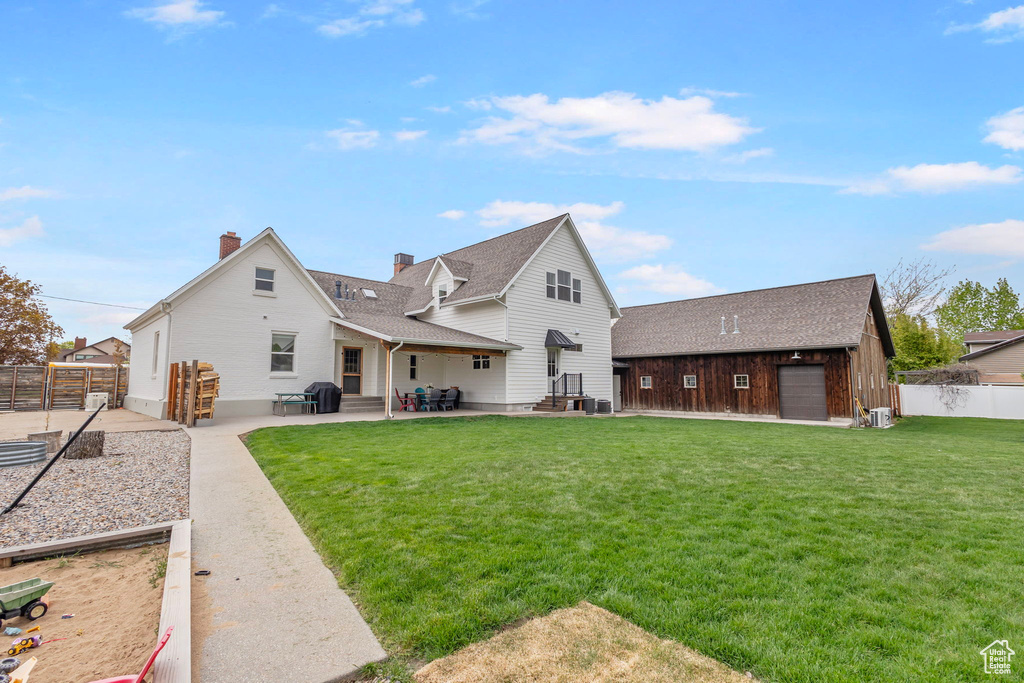 Rear view of house with a lawn, fence, an outbuilding, and a patio area