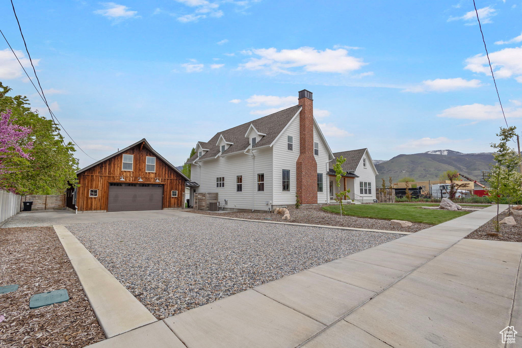 View of front of property with fence, a front lawn, an outdoor structure, a detached garage, and a mountain view
