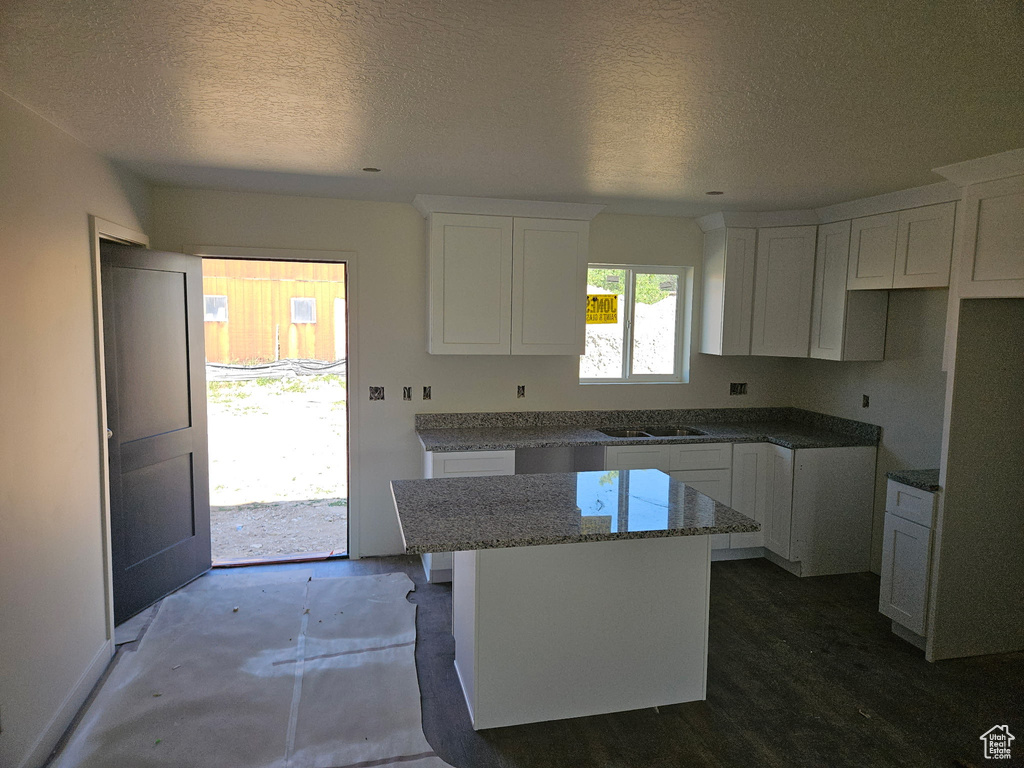Kitchen with a kitchen island, a textured ceiling, white cabinetry, and stone countertops