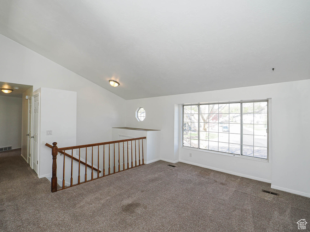 Spare room with vaulted ceiling, visible vents, and carpet flooring