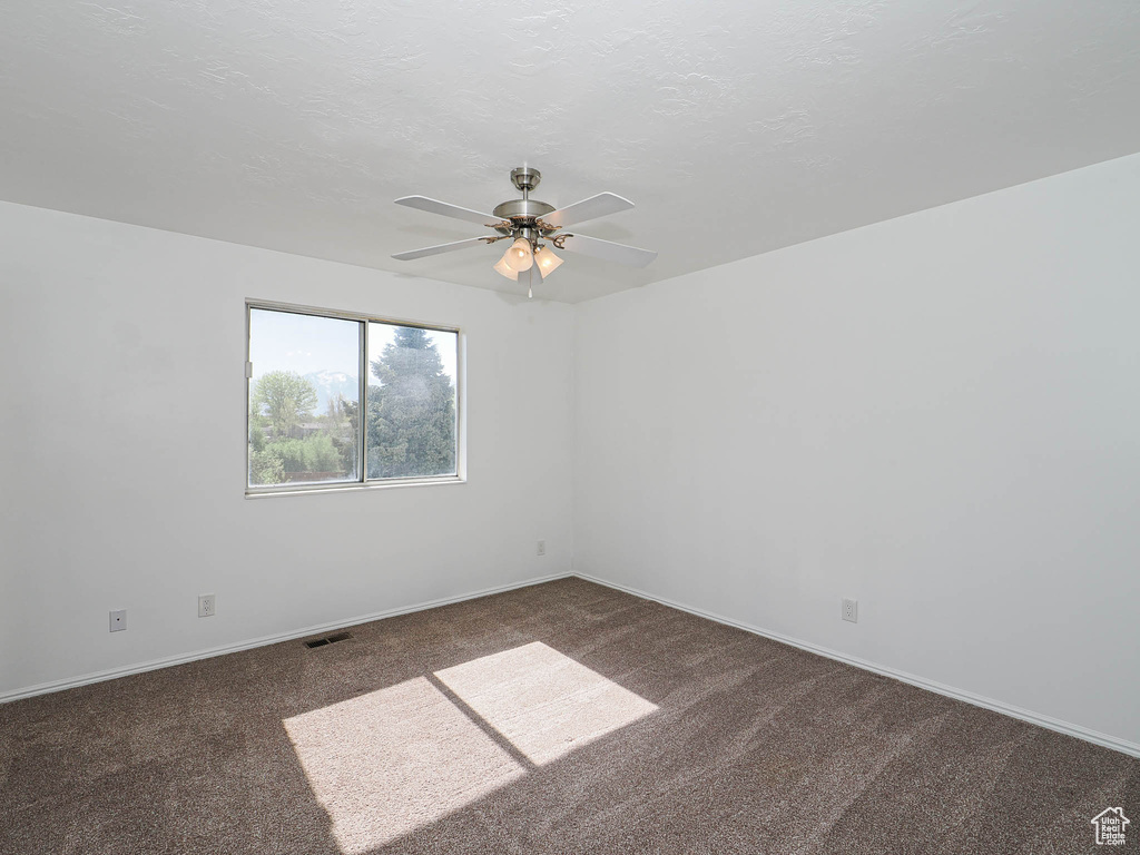 Carpeted spare room featuring visible vents, a ceiling fan, and baseboards