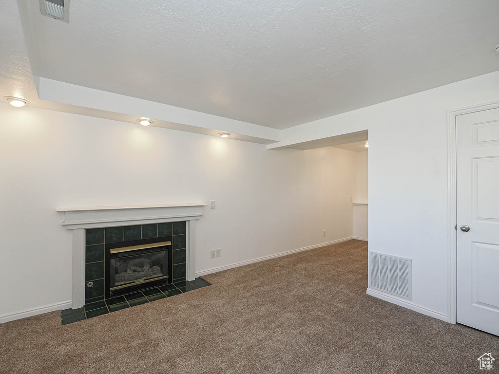 Unfurnished living room featuring baseboards, carpet flooring, a tile fireplace, and visible vents