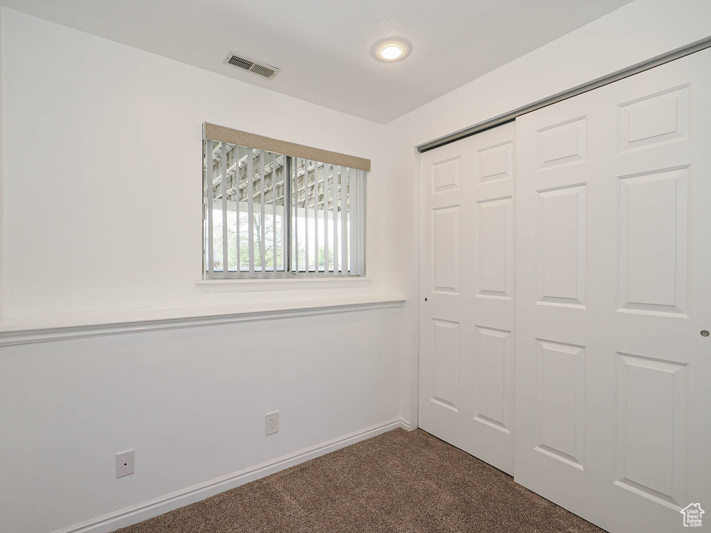 Unfurnished bedroom featuring baseboards, dark colored carpet, visible vents, and a closet