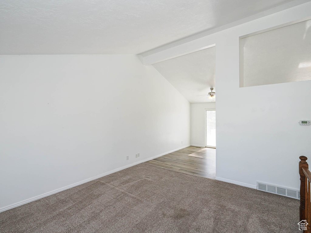 Empty room with visible vents, carpet floors, baseboards, lofted ceiling with beams, and ceiling fan
