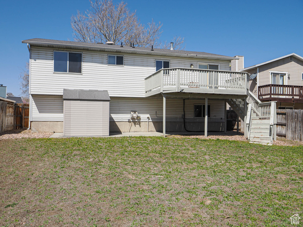 Back of property with a shed, a deck, a fenced backyard, an outdoor structure, and a yard