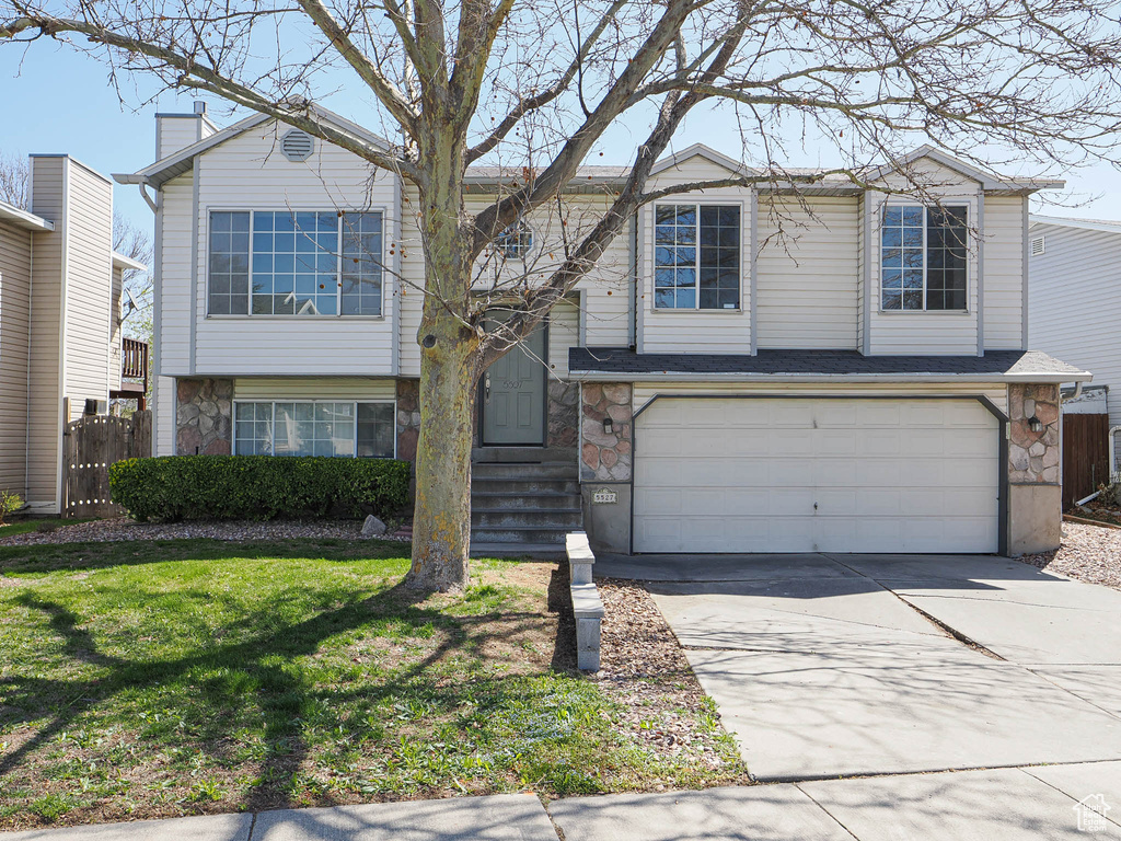 Raised ranch with concrete driveway, fence, stone siding, and a garage