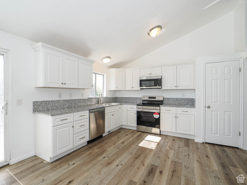 Kitchen with lofted ceiling, white cabinets, a sink, and appliances with stainless steel finishes