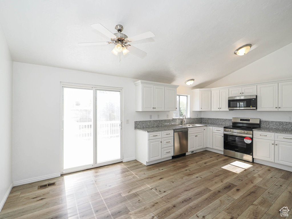 Kitchen with a sink, light wood-type flooring, stainless steel appliances, white cabinets, and lofted ceiling