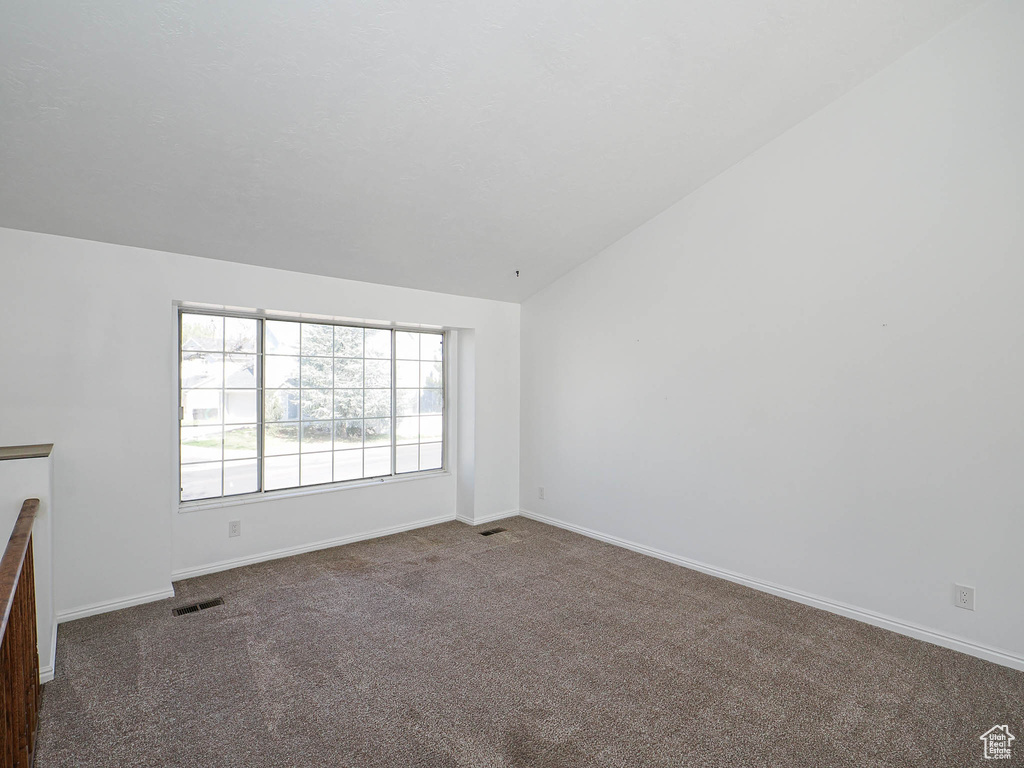 Spare room featuring baseboards, lofted ceiling, visible vents, and carpet