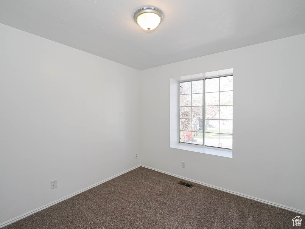 Unfurnished room with dark colored carpet, visible vents, and baseboards