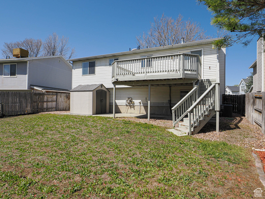 Back of property with a storage shed, an outbuilding, a fenced backyard, a wooden deck, and a yard