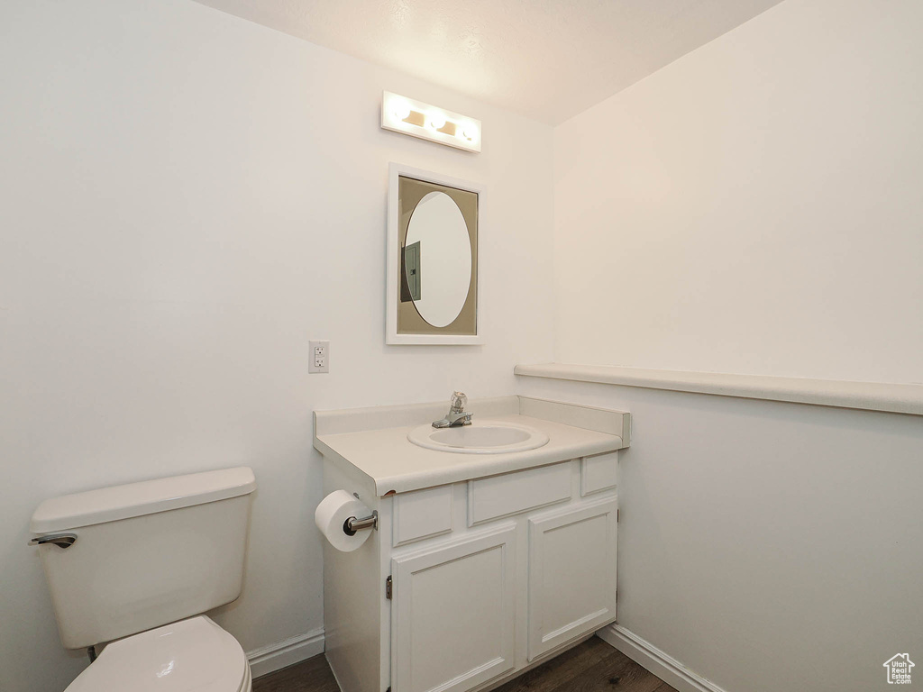 Half bathroom with baseboards, toilet, vanity, and wood finished floors