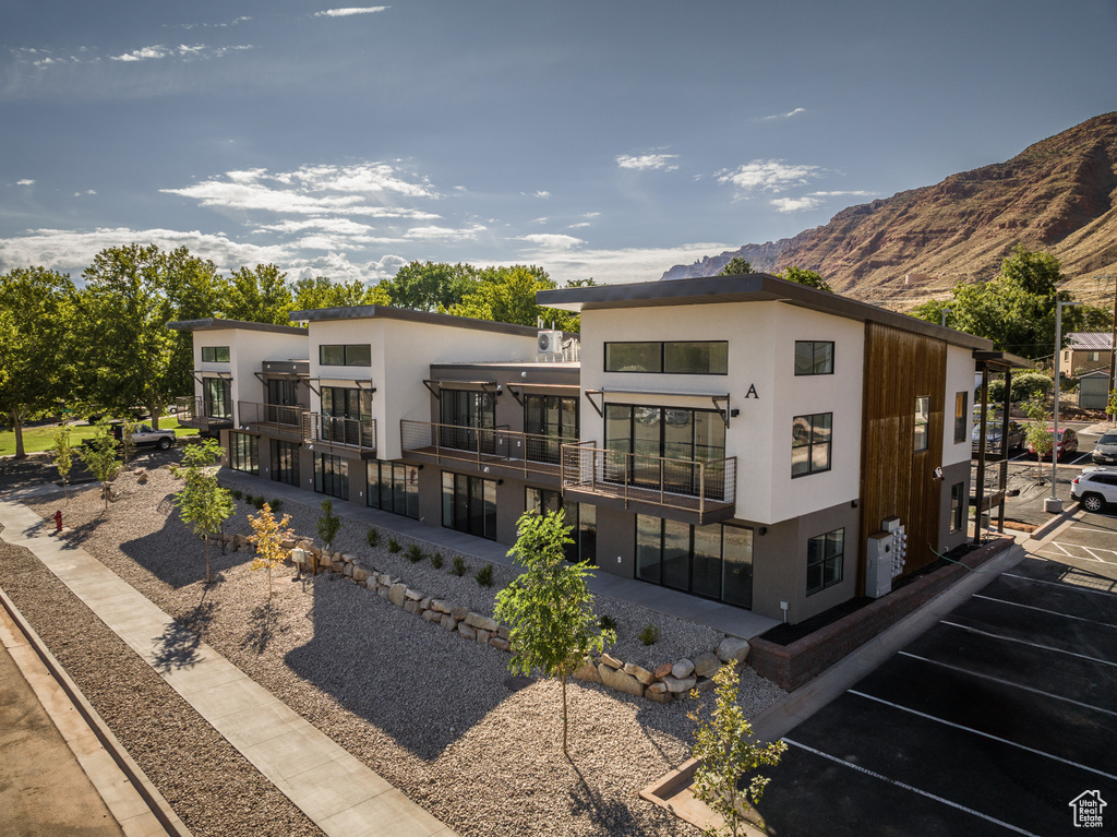 Rear view of house featuring a balcony, uncovered parking, a mountain view, and stucco siding