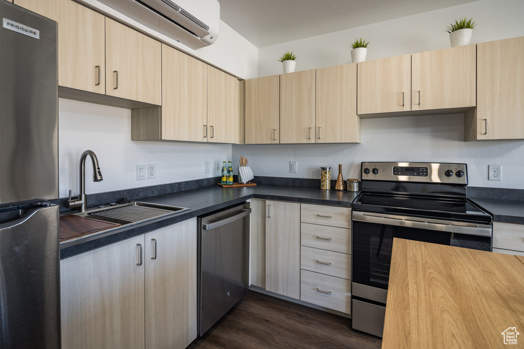 Kitchen featuring light brown cabinetry, appliances with stainless steel finishes, dark wood-style flooring, and a sink