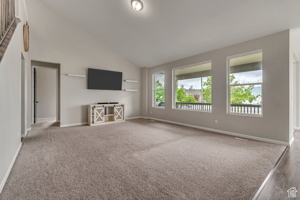 Unfurnished living room with baseboards, wood finished floors, and high vaulted ceiling