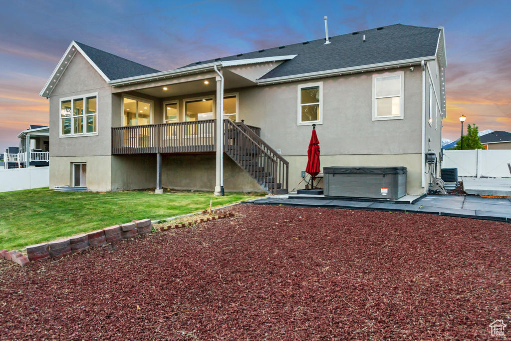 Rear view of house with a hot tub, stucco siding, a patio, and central AC