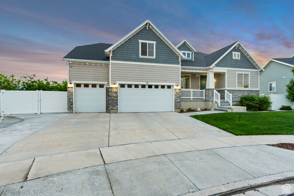 Craftsman inspired home featuring stone siding, covered porch, driveway, and a gate