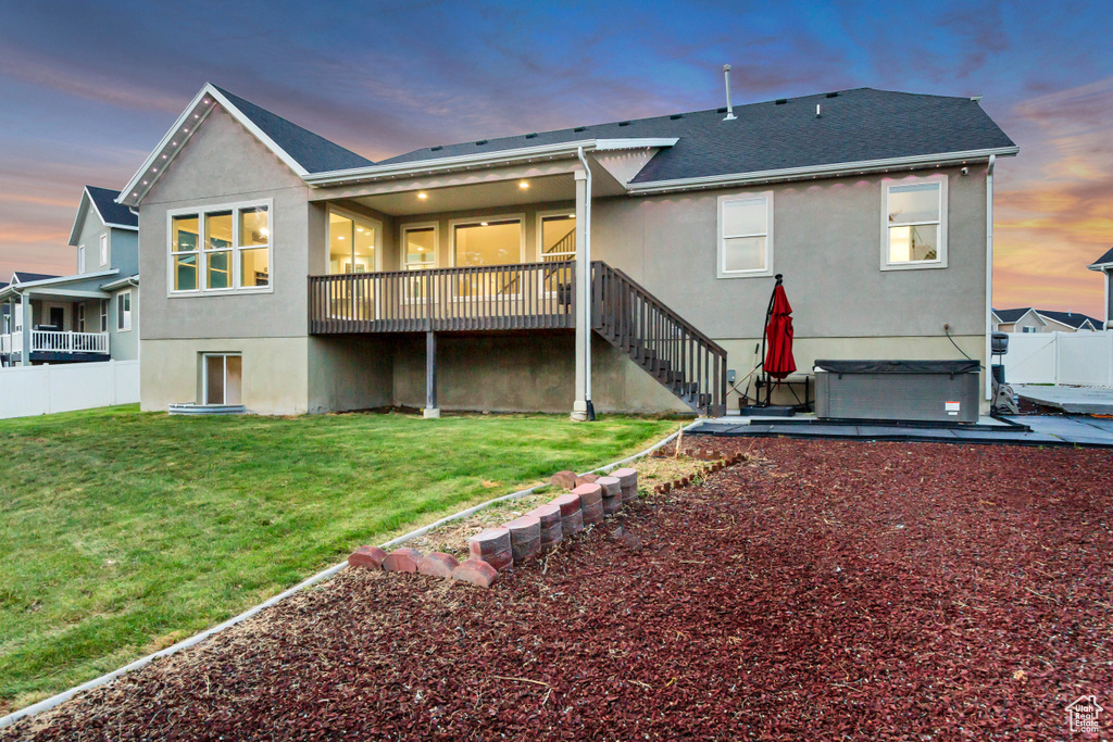 Back of house at dusk featuring a hot tub, stucco siding, a wooden deck, stairway, and roof with shingles