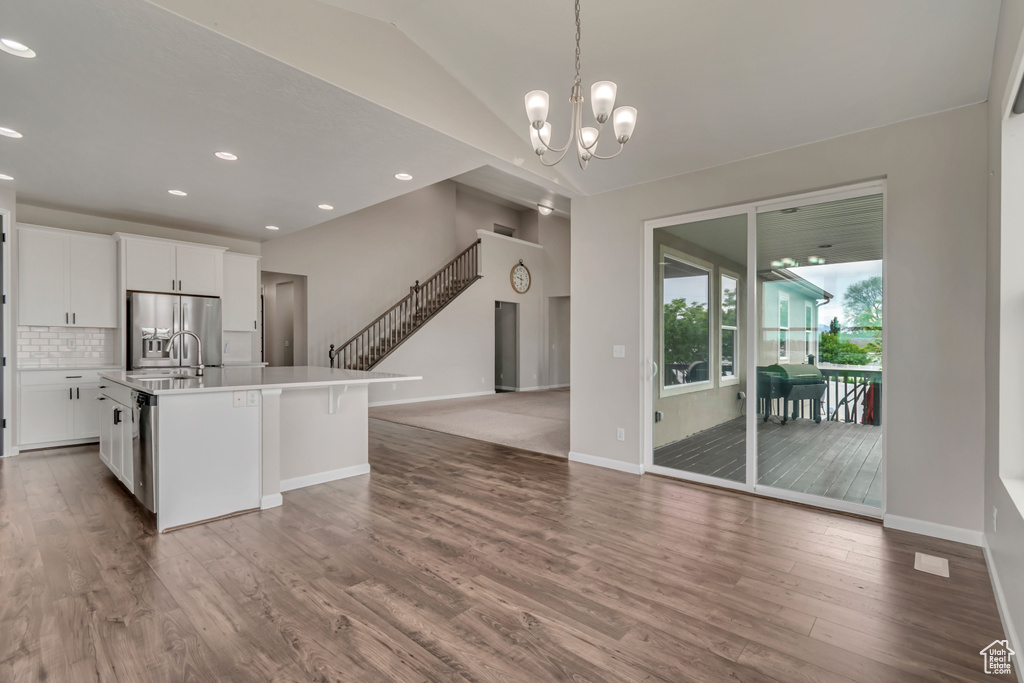Kitchen with stainless steel fridge, a chandelier, wood finished floors, decorative backsplash, and open floor plan