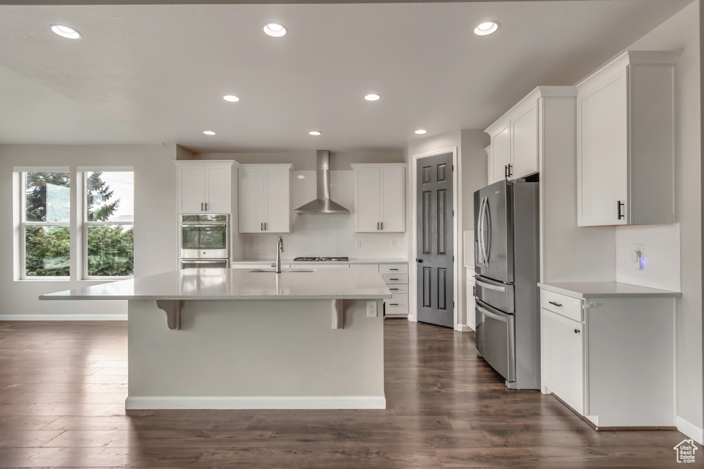 Kitchen with wall chimney exhaust hood, appliances with stainless steel finishes, a sink, tasteful backsplash, and dark wood-type flooring