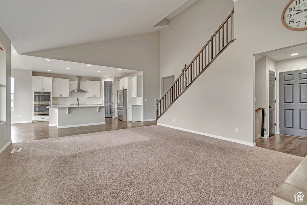 Unfurnished living room featuring dark colored carpet, high vaulted ceiling, a sink, baseboards, and stairway