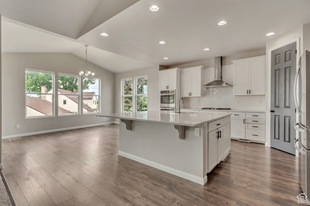 Kitchen with wall chimney exhaust hood, a sink, stainless steel appliances, dark wood finished floors, and lofted ceiling