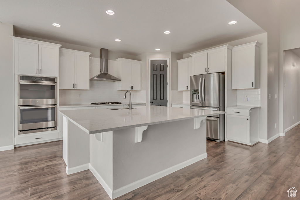 Kitchen featuring wall chimney range hood, stainless steel appliances, white cabinets, decorative backsplash, and recessed lighting