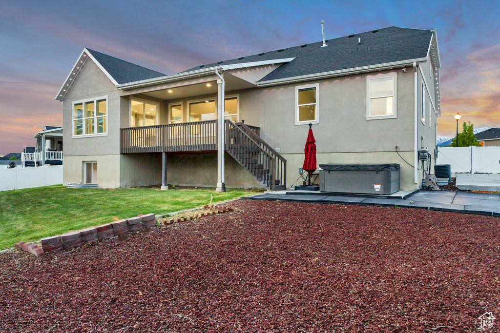 Back of house at dusk featuring a hot tub, stucco siding, a patio area, stairway, and central air condition unit