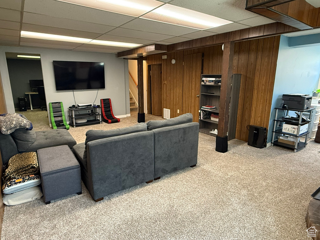 Living area with wooden walls, stairway, light colored carpet, and a drop ceiling