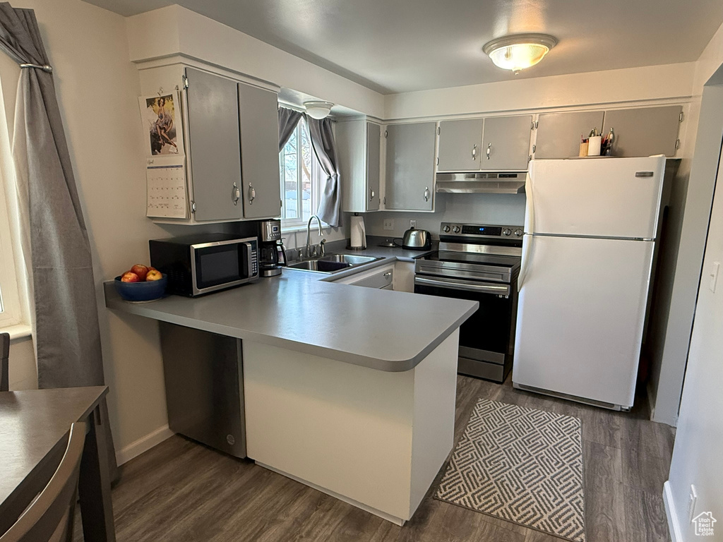 Kitchen with a sink, stainless steel appliances, a peninsula, range hood, and dark wood-style floors