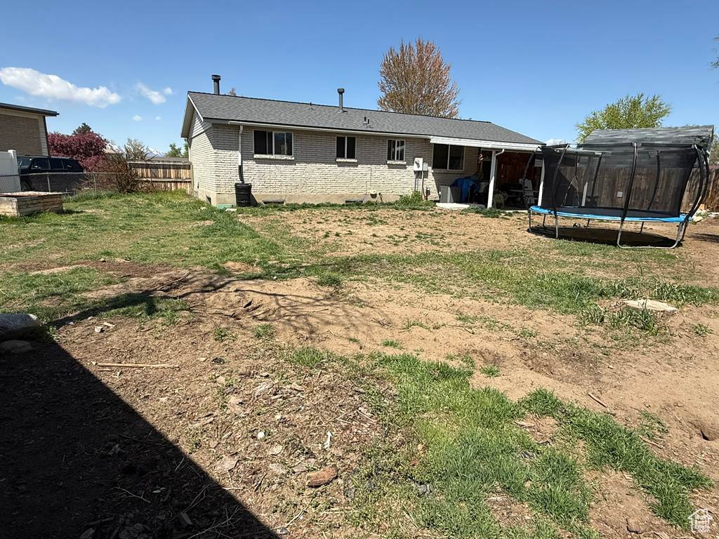 Back of property featuring brick siding, a trampoline, a lawn, and a fenced backyard