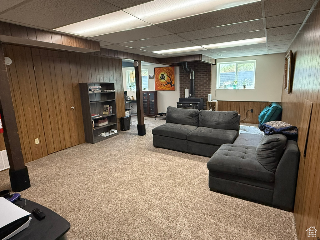 Living area with carpet floors, a wood stove, wood walls, and a drop ceiling