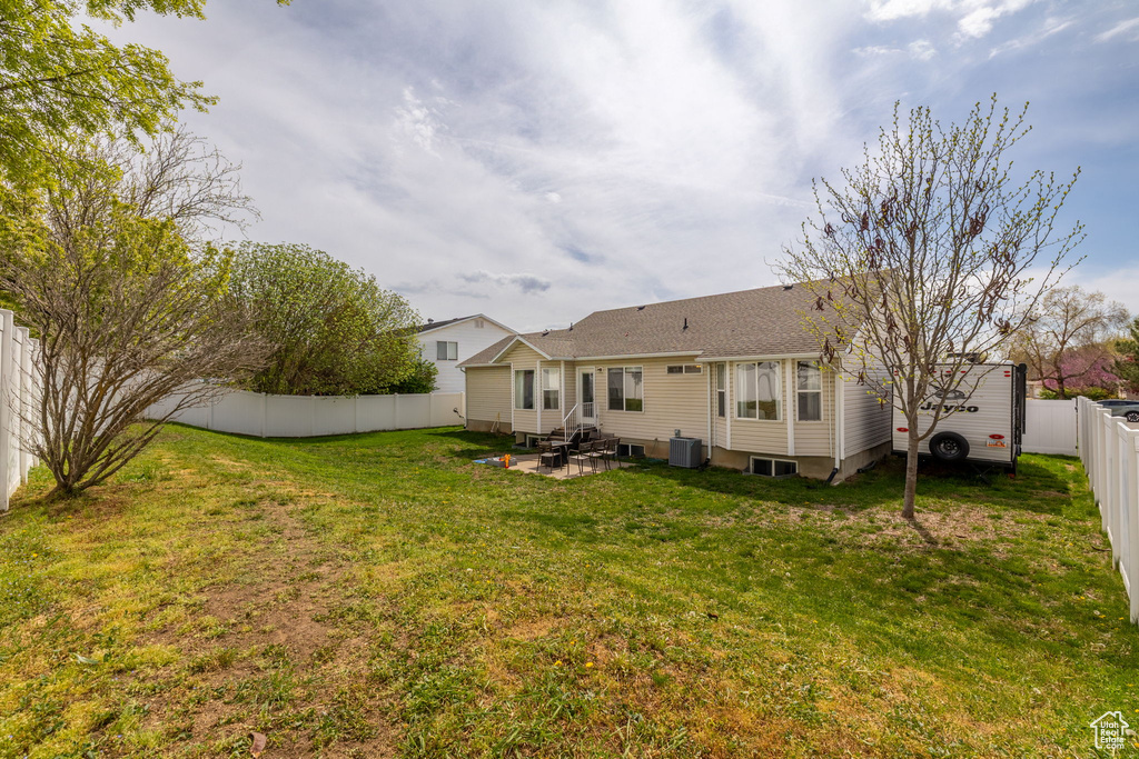 Rear view of house featuring central AC unit, a fenced backyard, entry steps, a patio, and a lawn