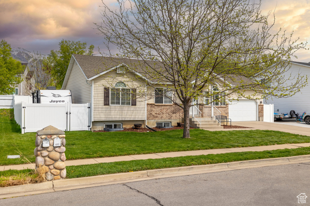 View of front of home with a gate, concrete driveway, fence, a garage, and a lawn