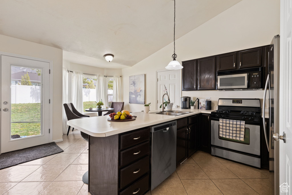 Kitchen with vaulted ceiling, a sink, light tile patterned flooring, a peninsula, and appliances with stainless steel finishes