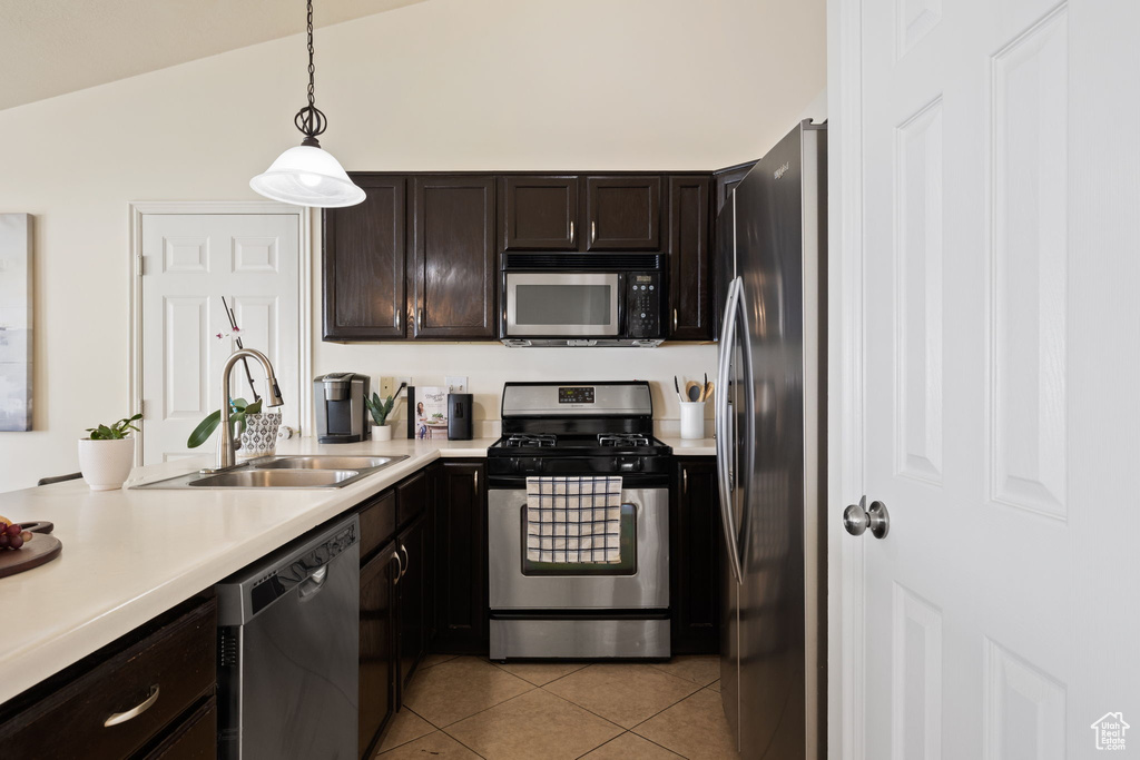 Kitchen with stainless steel appliances, a sink, dark brown cabinetry, light countertops, and light tile patterned floors