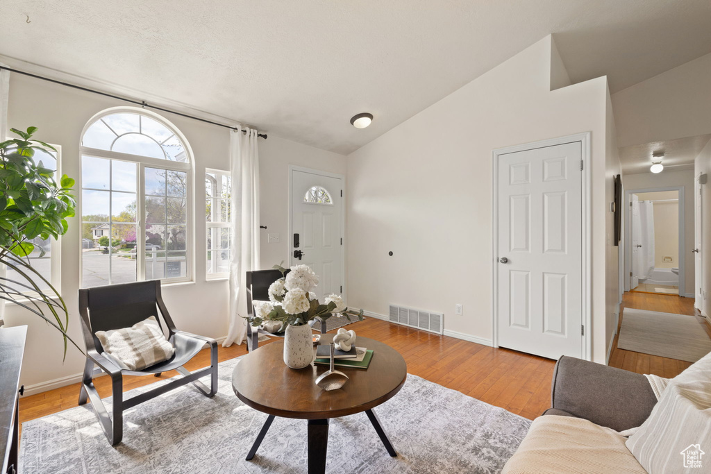 Living room featuring wood finished floors, baseboards, vaulted ceiling, and visible vents