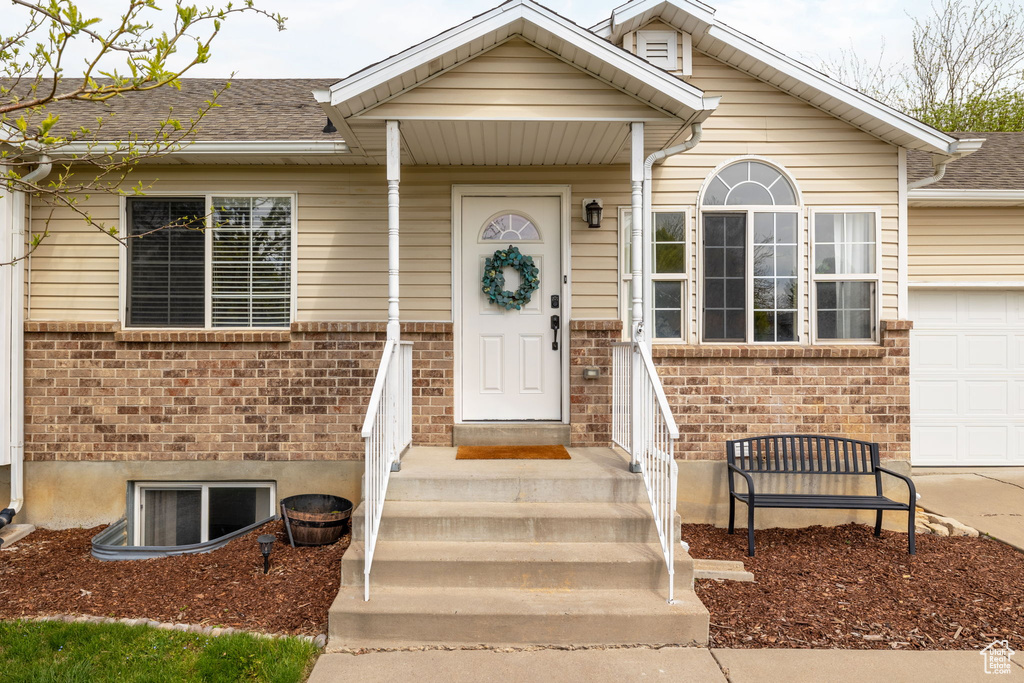 Property entrance featuring an attached garage, a shingled roof, brick siding, and concrete driveway