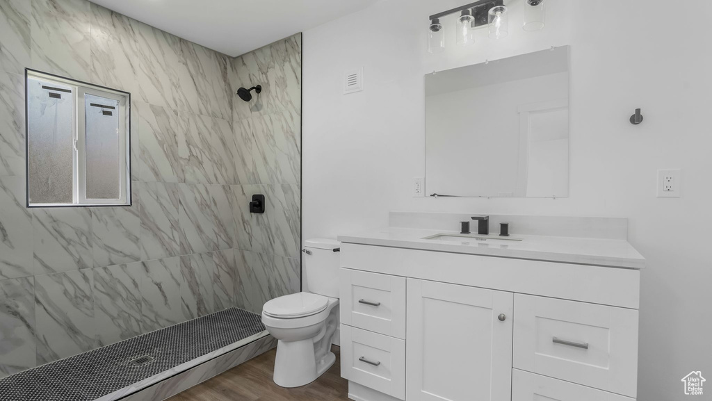 Full bathroom with a tile shower, toilet, vanity, and wood finished floors