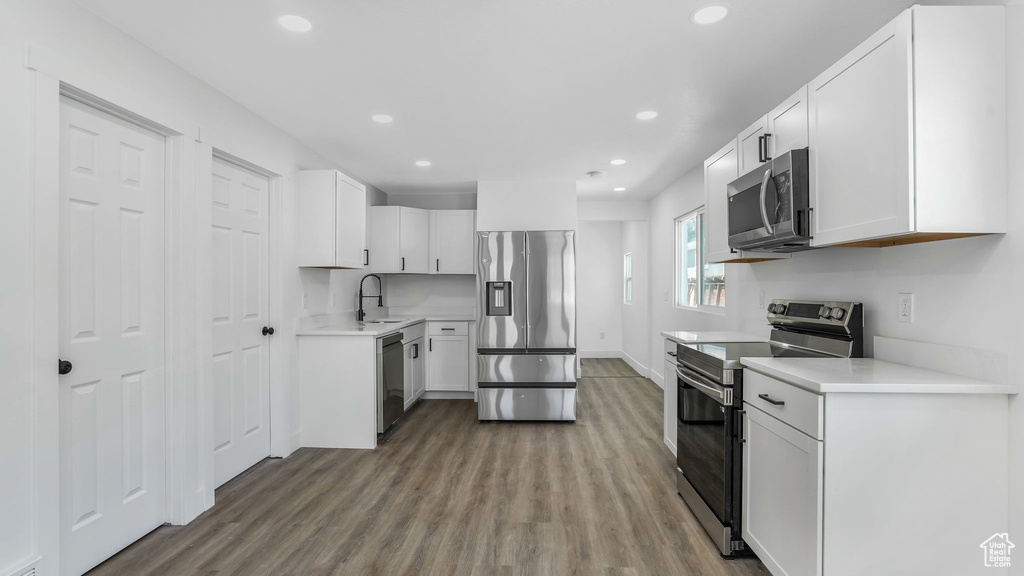 Kitchen with white cabinets, stainless steel appliances, a sink, recessed lighting, and wood finished floors