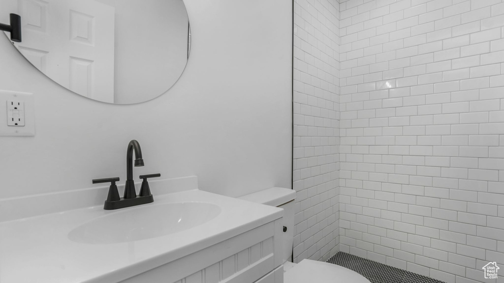 Bathroom featuring a tile shower, toilet, and vanity