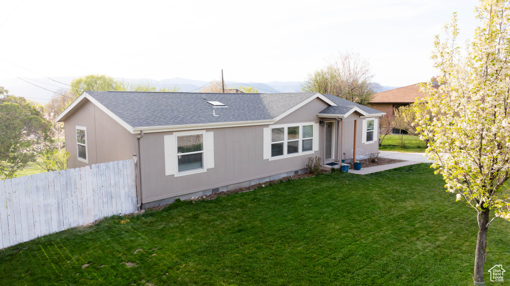 Rear view of property featuring a lawn, fence, a shingled roof, and a mountain view