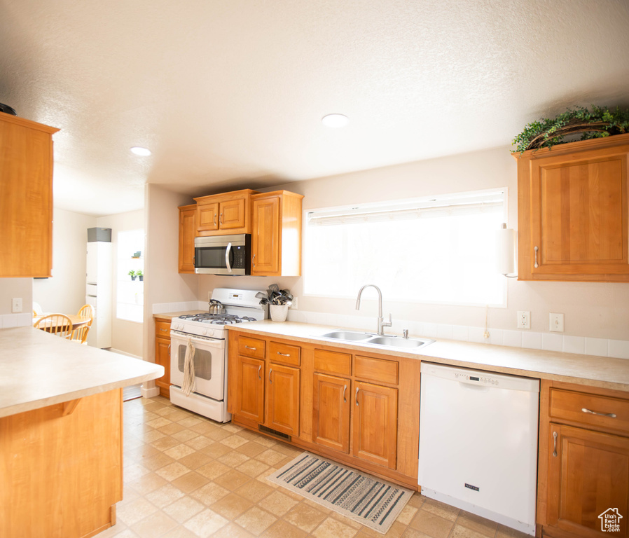 Kitchen featuring a wealth of natural light, light countertops, white appliances, and a sink