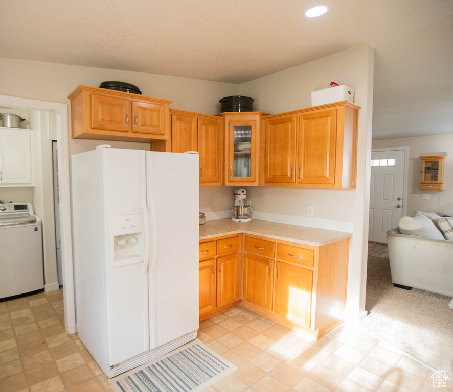 Kitchen with light floors, light countertops, white fridge with ice dispenser, glass insert cabinets, and washer / clothes dryer