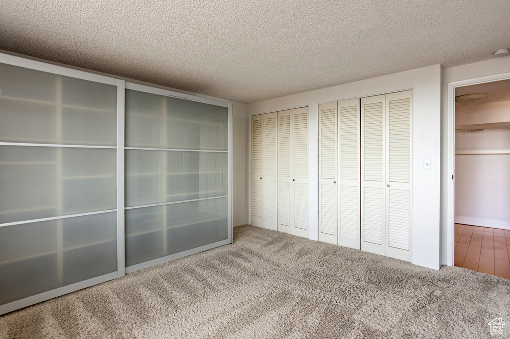 Unfurnished bedroom with two closets, carpet flooring, and a textured ceiling