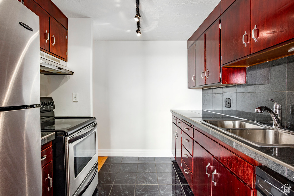 Kitchen featuring stainless steel appliances, under cabinet range hood, tasteful backsplash, track lighting, and dark tile patterned flooring